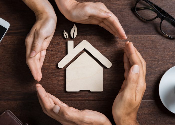 House care Top view of hands of a couple protecting their ecologigal house on wooden background. High angle view of hand of man and woman covering house shape. New home, Insurance and security concept.